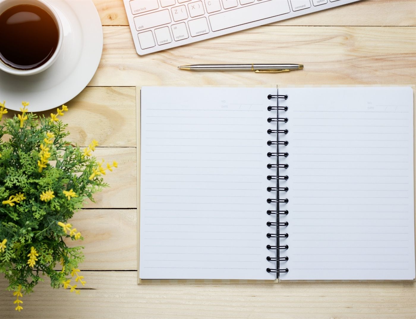 Aufgeschlagenes Notizbuch, Kaffee und Tastatur auf einem Holztisch