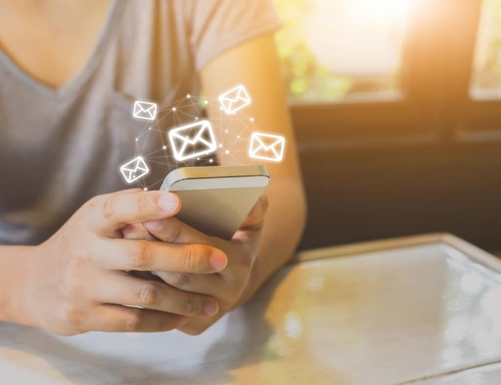 Hände halten ein Smartphone, darüber schweben E-Mail-Symbole