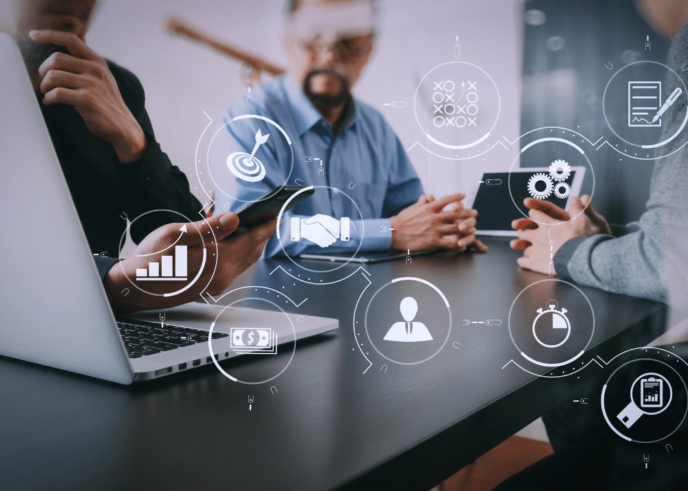 Drei Personen besprechen am Tisch ihre Marketing-Automatisierung, darüber schweben Symbole Drei Personen besprechen am Tisch ihre Marketing-Automatisierung, darüber schweben Symbole